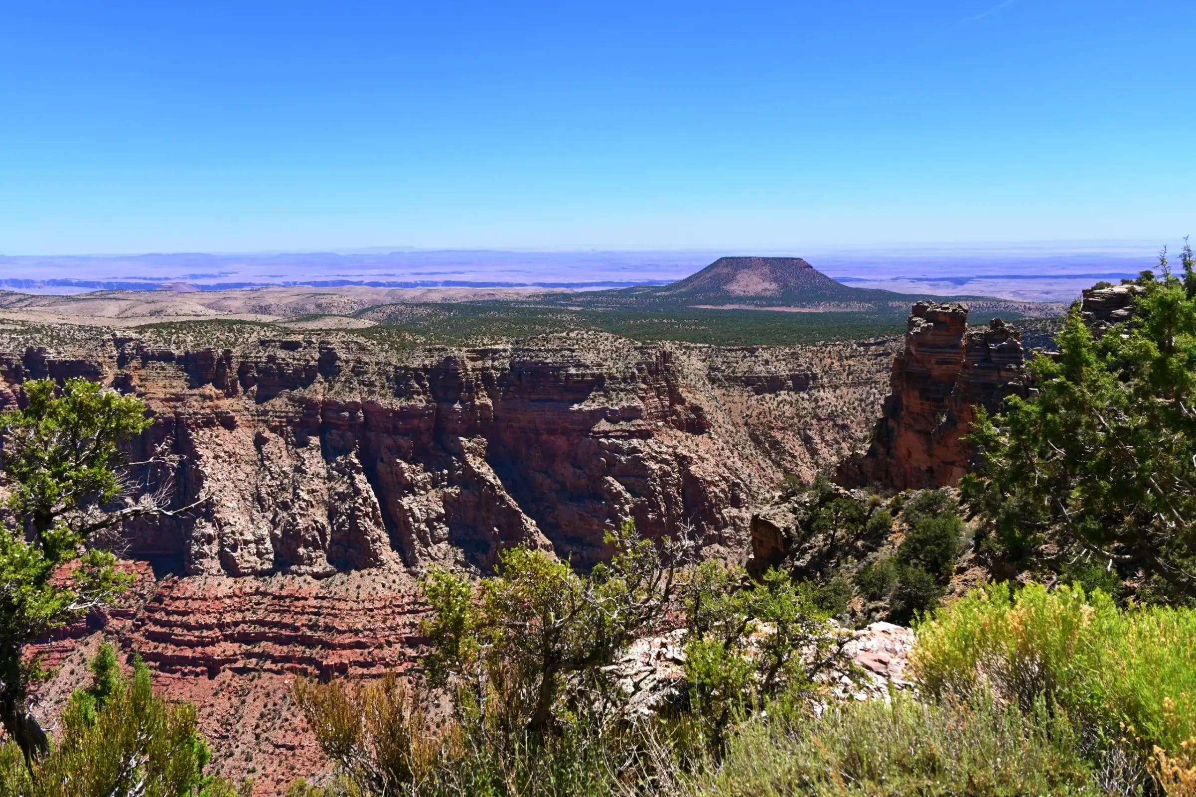 A wide desert landscape beyond the canyon rim, marked by a distant volcanic cone